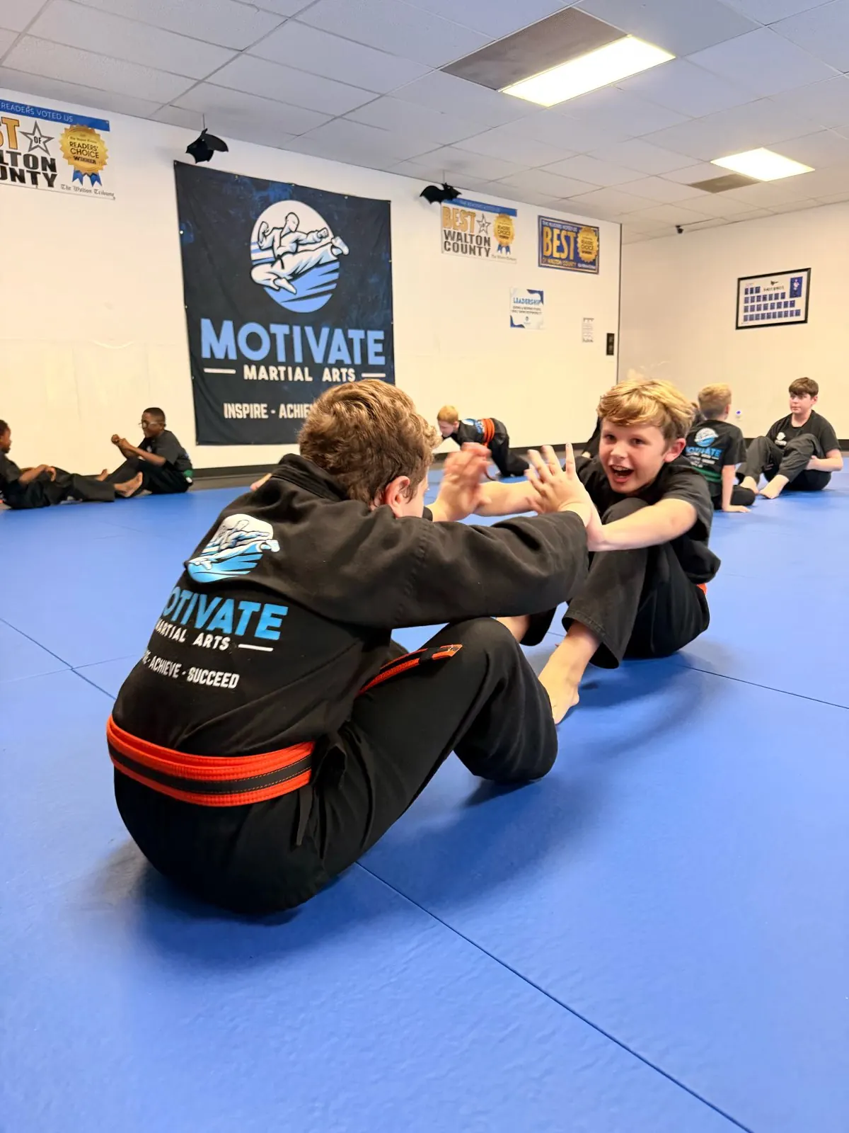 Two smiling Junior TaeKwonDo students doing partner sit-ups on the blue mats