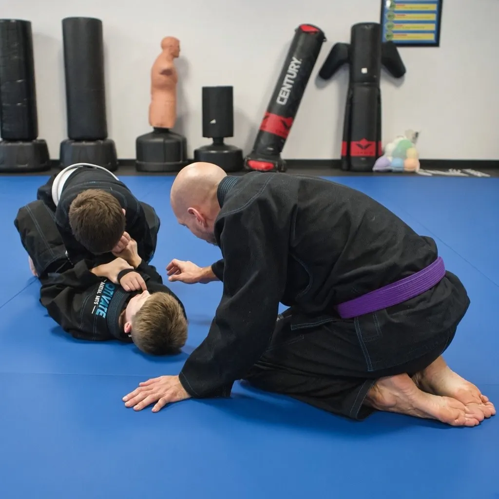 A coach showing two Juniors BJJ students a position on the blue mats